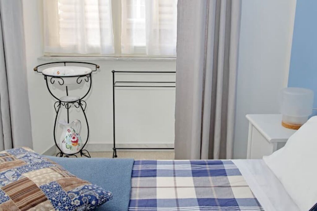 A bedroom with a bed, a bedside table, a window with curtains, and a radiator.