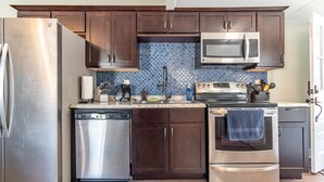 A modern kitchen with stainless steel appliances, dark wooden cabinets, and a blue patterned backsplash.