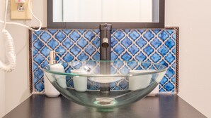 A bathroom with a glass vessel sink, a mirror, and a blue patterned backsplash.