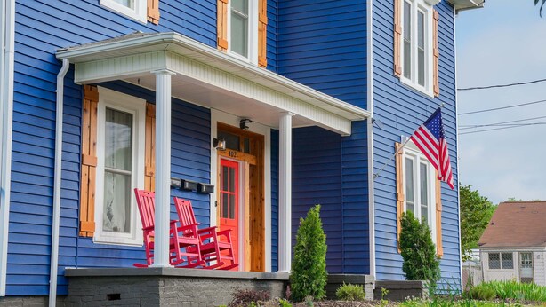 A blue house with a porch, a red door, and an American flag.