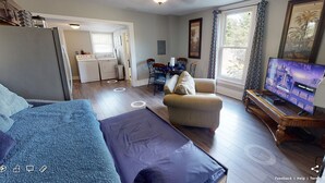 A living room with a sofa, armchair, TV, and a dining area with chairs and a table.
