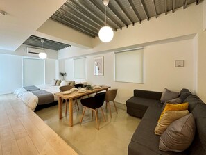 A modern, well-lit living room with a dining area, a sofa, and a bed. - Arts Dobashi (Hiroshima)
