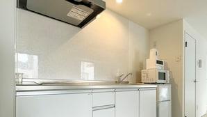 A modern kitchen with white cabinets, a stainless steel range hood, and a microwave. - Arts Dobashi (Hiroshima)