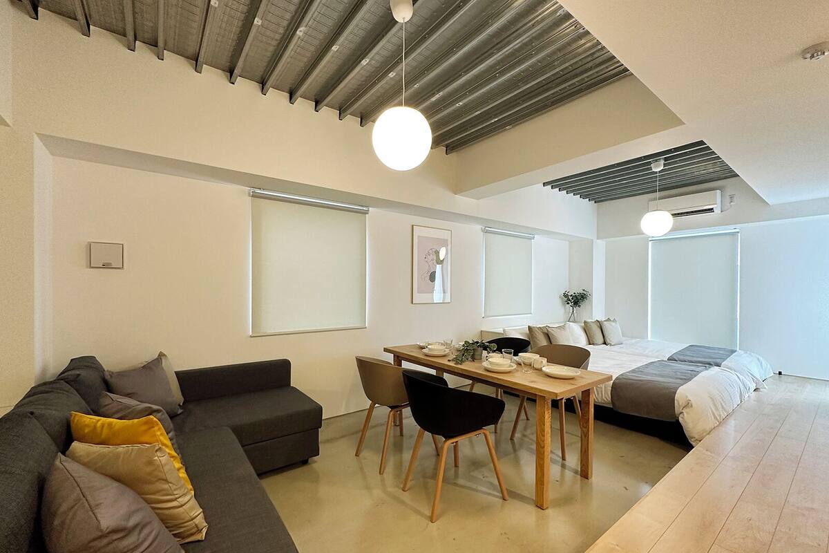 A modern, well-lit living area with a sofa, dining table, and a bed.