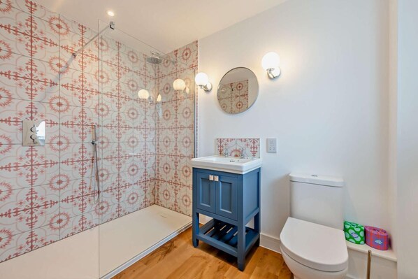 A bathroom with patterned tiles, a shower, a sink with a mirror, and a toilet.