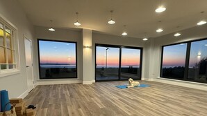 Una habitación espaciosa con ventanas grandes, piso de madera y un perro descansando sobre una alfombra.