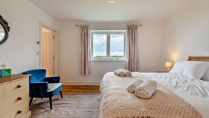 Un dormitorio con cama, una silla, cómoda, ventana con cortinas y lámpara colgante.