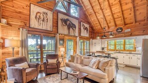 A spacious living room with a high ceiling, wooden walls, and large windows. There is a sofa, a chair, and a coffee table. - 2 King BR with Loft, Mountain Views & Hot Tub (Blue Ridge)