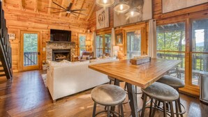 A rustic cabin interior with a stone fireplace, wooden dining table, and a cozy seating area. - 2 King BR with Loft, Mountain Views & Hot Tub (Blue Ridge)