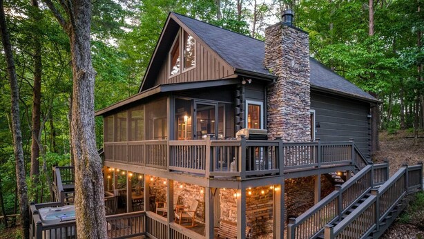 A two-story cabin with a stone chimney, wooden deck, and outdoor seating area. - 2 King BR with Loft, Mountain Views & Hot Tub (Blue Ridge)