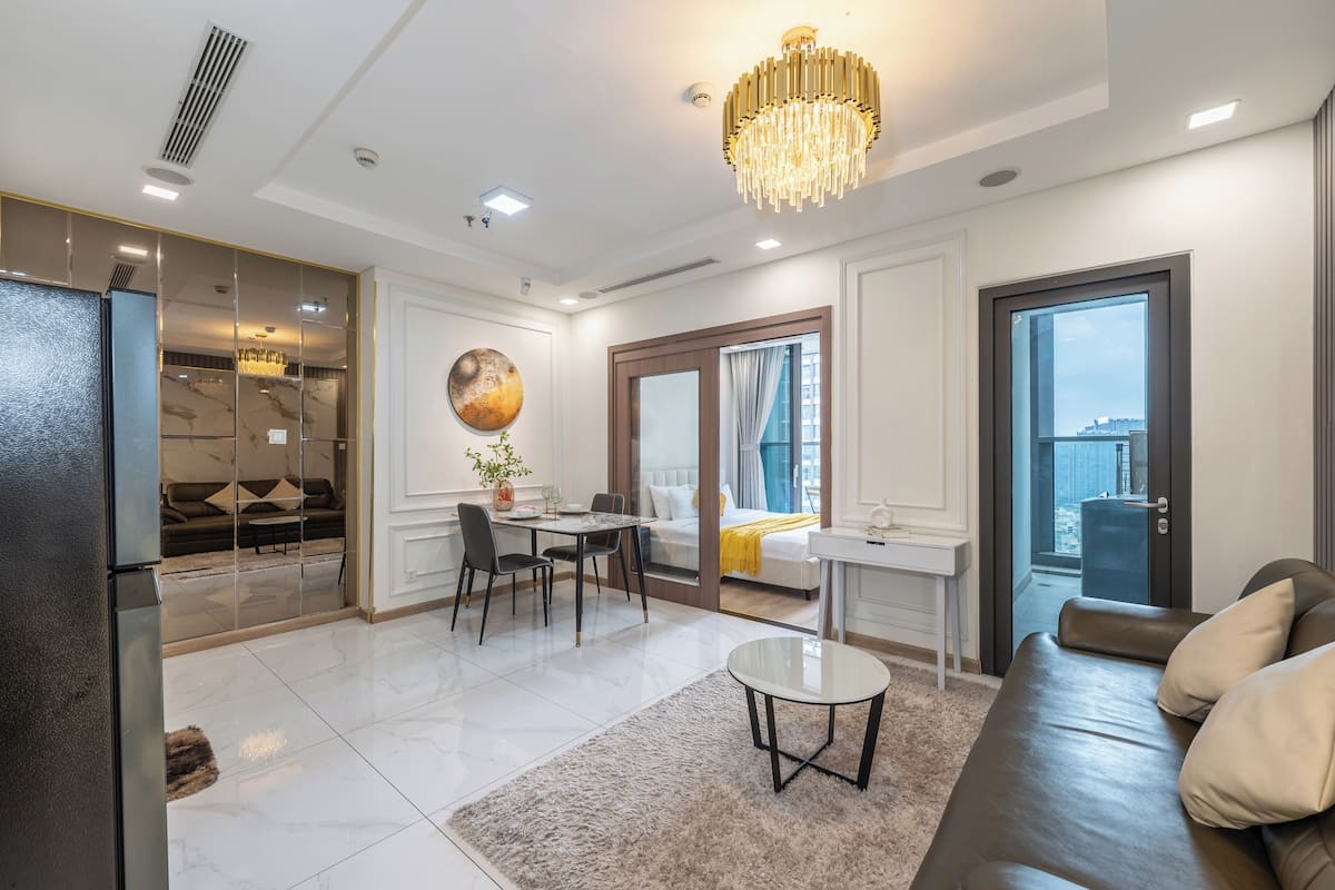 Un salon moderne comprenant un coin repas, un canapé, un lustre et une vue dégagée sur l’extérieur grâce à une grande fenêtre.