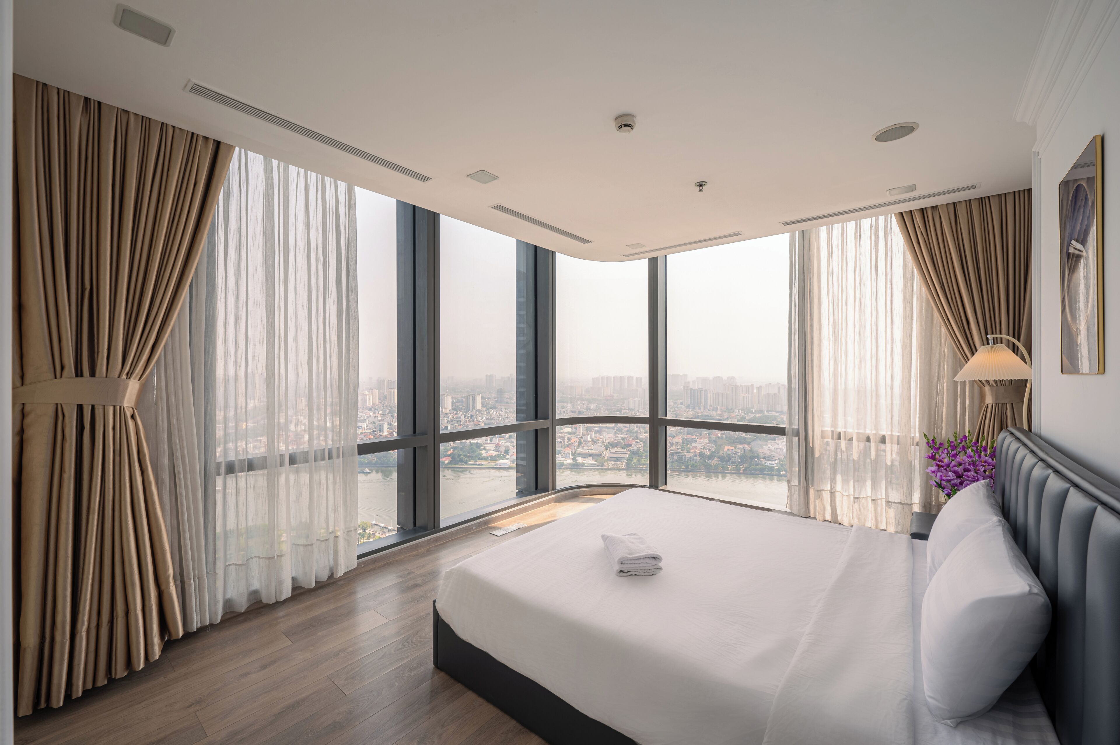 A modern hotel room with a large bed, a view of a cityscape, and a balcony.