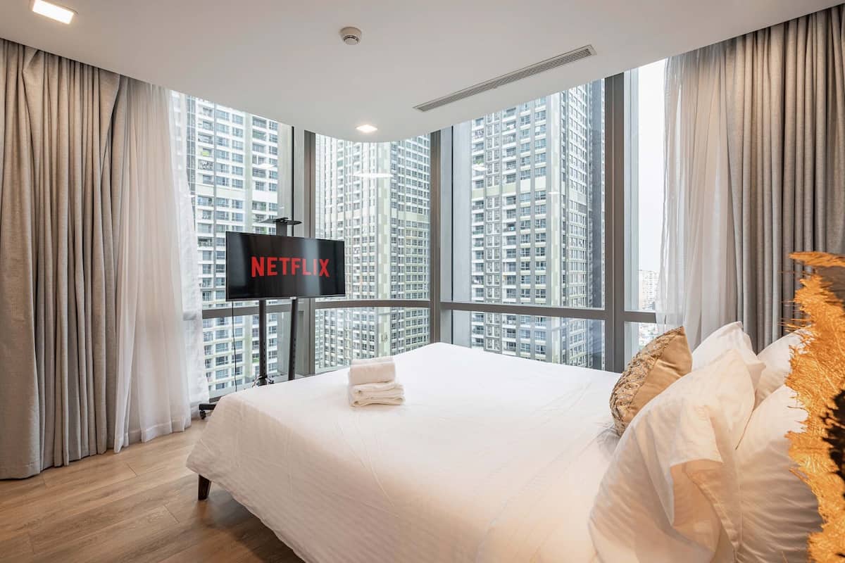 Une chambre d’hôtel avec un grand lit, un téléviseur fixé au mur et une vue sur des immeubles de grande hauteur.