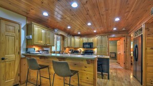 L’intérieur d’une cabane en bois comprend une cuisine équipée de meubles en bois, d’un îlot central avec des tabourets de bar et d’un réfrigérateur.