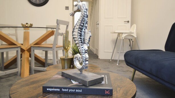 Et værelse med spisebord, stole, sofa, en dekorativ metalkulptur og en bog med titlen 'Wagamama feed your soul'.