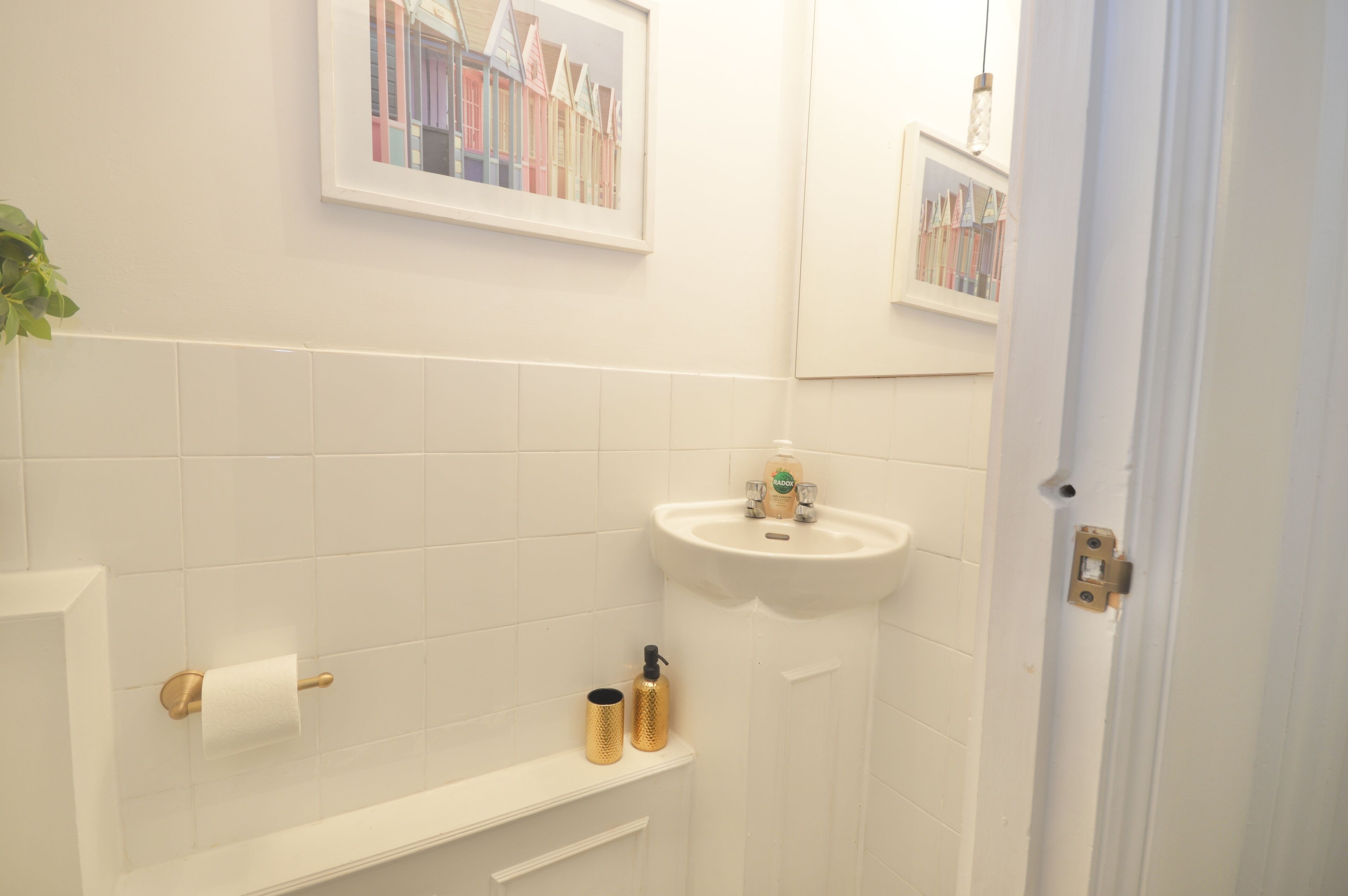 A bathroom with white tiles, a sink, a toilet paper holder, and a shelf with toiletries.