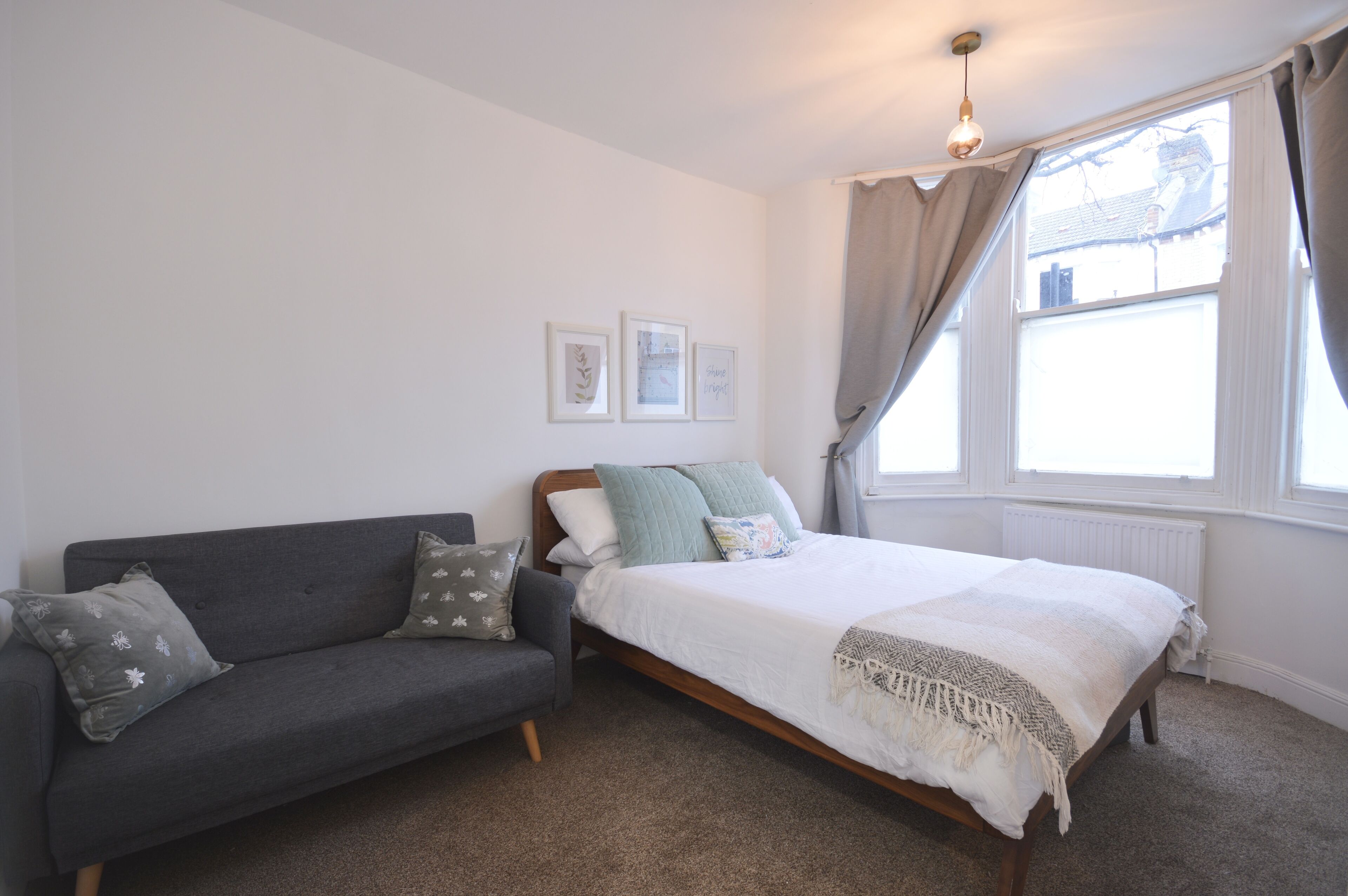 A bedroom with a bed, a grey sofa, and a window with curtains.