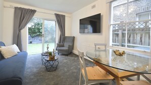 En moderne stue med en blå sofa, en grå lænestol, et glasbord og et fjernsyn monteret på væggen.