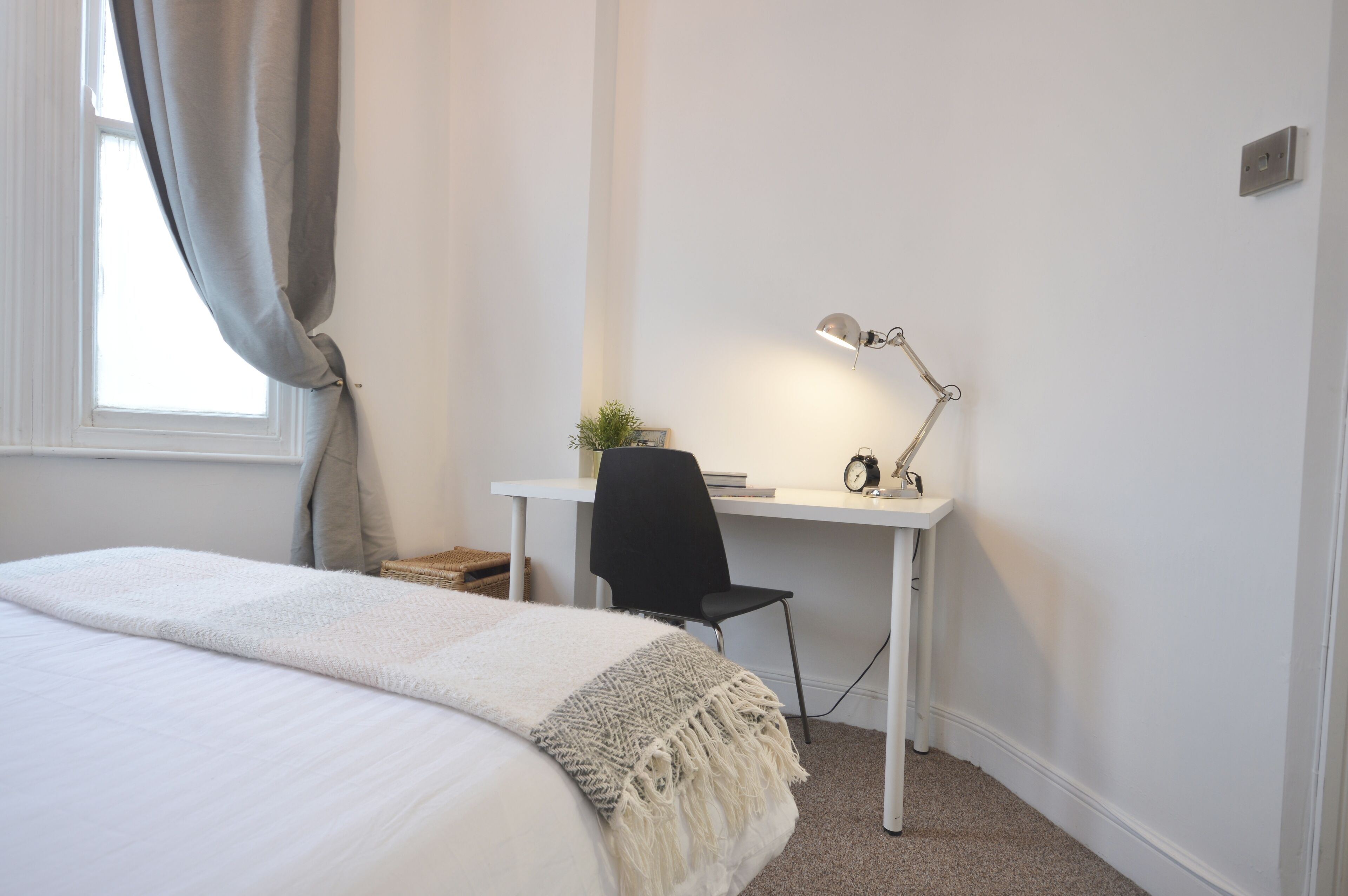A bedroom with a bed, a desk, a chair, and a lamp.