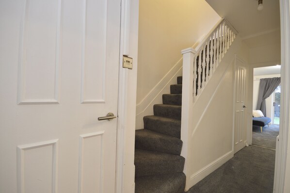 A hallway with a carpeted staircase, white doors, and a bed in the background.