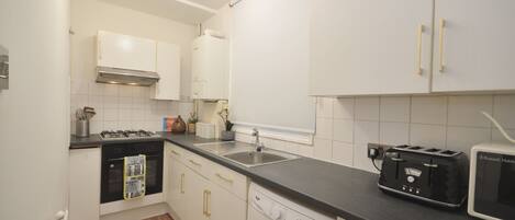 A compact kitchen with white cabinets, a gas stove, a washing machine, and a toaster.