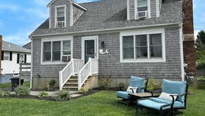 A two-story house with a front porch, a chimney, and a small garden with outdoor furniture. - 88 Town Neck Road (Sandwich)