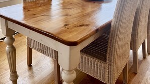 A dining table with wicker chairs, a framed picture on the wall, and a view of the outdoors through large windows. - 88 Town Neck Road (Sandwich)