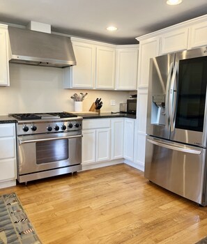 A modern kitchen with white cabinetry, stainless steel appliances, and a wooden floor.