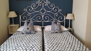 A double bed with a decorative metal headboard, two bedside tables with lamps, patterned bedding, and two wall-mounted picture frames.