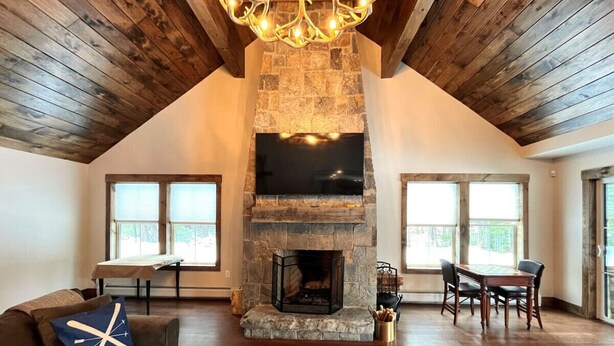 Un salón espacioso con chimenea de piedra, vigas de madera en el techo y ventanas amplias.