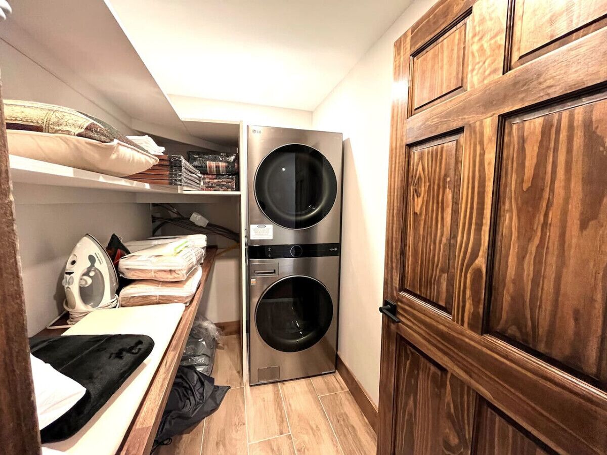 A compact laundry room with two stacked front-loading washing machines, a drying rack, and a wooden wardrobe.