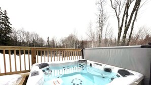 Un jacuzzi en una terraza de madera con barandilla de madera y árboles al fondo.