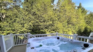 Een hottub op een houten terras met witte leuningen, omringd door bomen.