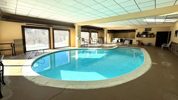 Una piscina interior con paredes de vidrio transparente, techo de baldosas y suelo de hormigón.
