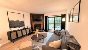 Una sala de estar moderna con un sofá modular, una mesa de centro, una chimenea y un televisor grande sobre un mueble negro.
