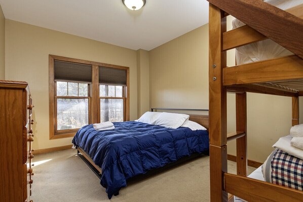 A bedroom with a bunk bed, a large window with blinds, a wooden dresser, and a carpeted floor. - Spectacular 4 Season Home on Spruce Lake (Wilmington)