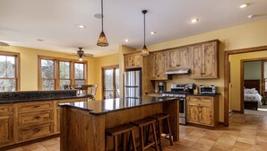 Cucina spaziosa con pensili in legno, un'isola grande con sgabelli e vista sull'esterno tramite ampie finestre.