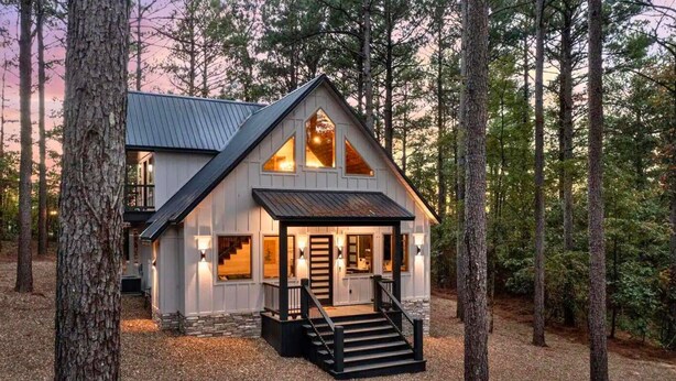 A cabin with a gabled roof, a front porch, and a staircase leading to the entrance. - Haus of Pine Cabin | Modern Woodland Cabin (Hochatown)