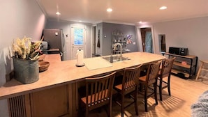 A compact kitchen with a central island, wooden chairs, and a potted plant. - New! Mt Snow Chalet w/land, privacy, relaxation (Dover)