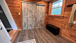 A room with wooden walls, a large barn-style door, a bench, a window with a view, and a patterned rug. - New! Mt Snow Chalet w/land, privacy, relaxation (Dover)