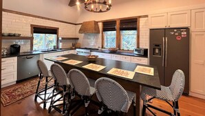 A modern kitchen with a central island, bar stools, a chandelier, and a refrigerator. - New! Min from Mt & Town. Hot tub, Stream + privacy (Wilmington)