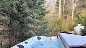 A hot tub in a forested area with a person standing beside it. - New! Min from Mt & Town. Hot tub, Stream + privacy (Wilmington)