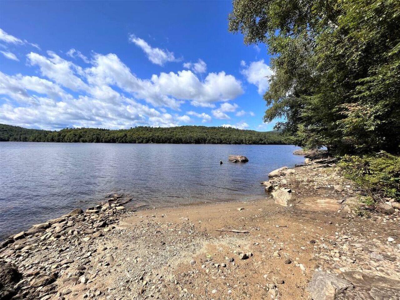 A rocky shoreline with a clear view of a lake and distant hills.