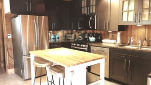 Een moderne keuken met donkere kasten, roestvrijstalen apparatuur, een houten eiland en barstoelen.
