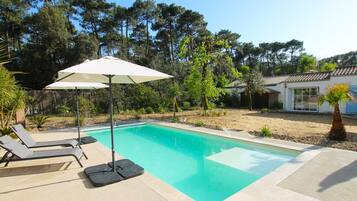 A swimming pool with lounge chairs and umbrellas, surrounded by trees and a house.