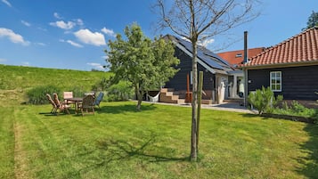 Une maison avec un toit recouvert de tuiles rouges, un porche à l’avant et un petit jardin agrémenté d’une table et de chaises pour prendre les repas.