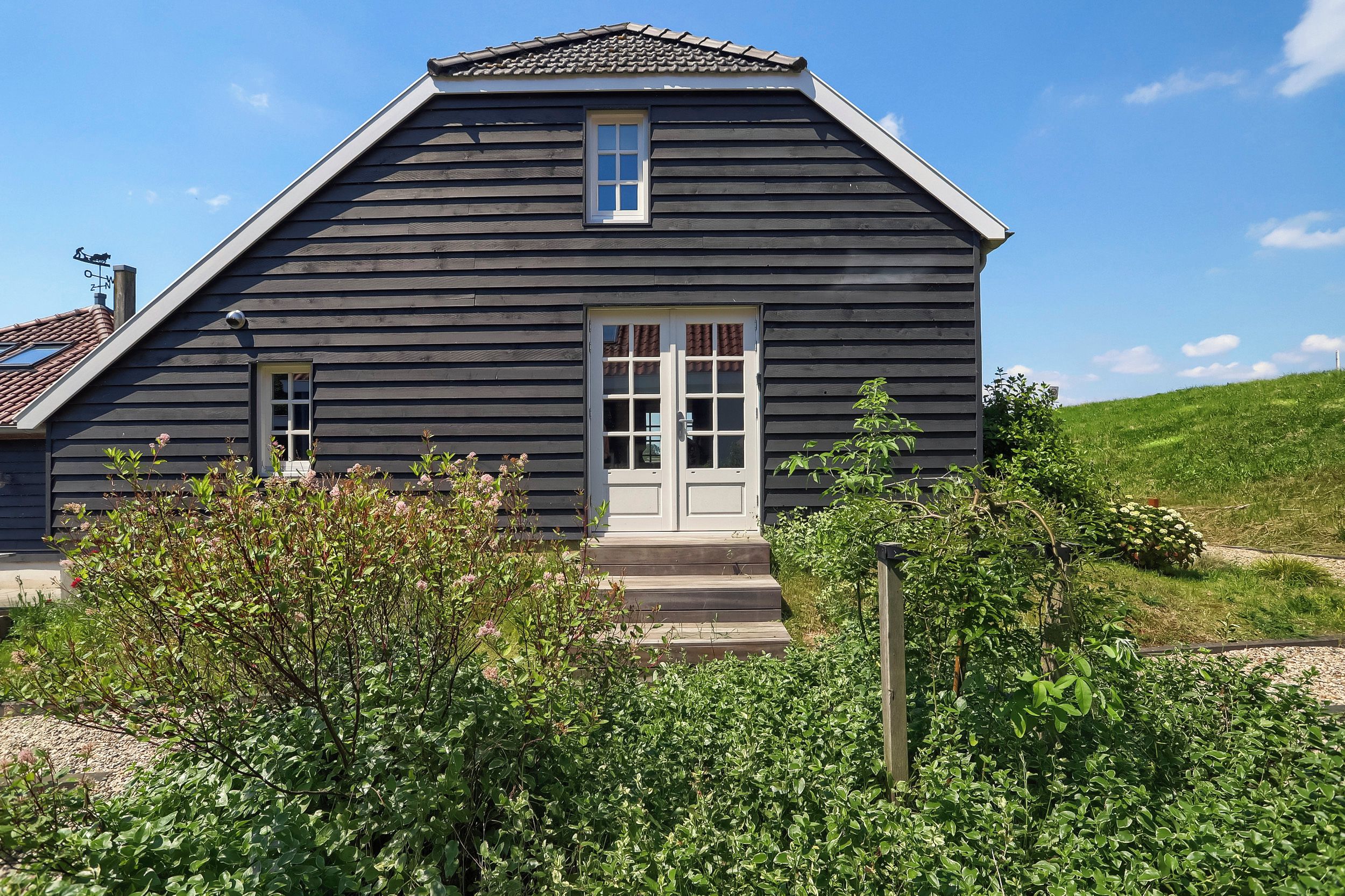 Een huis met twee verdiepingen, een steil zadeldak, een voordeur en een klein raam boven de deur.