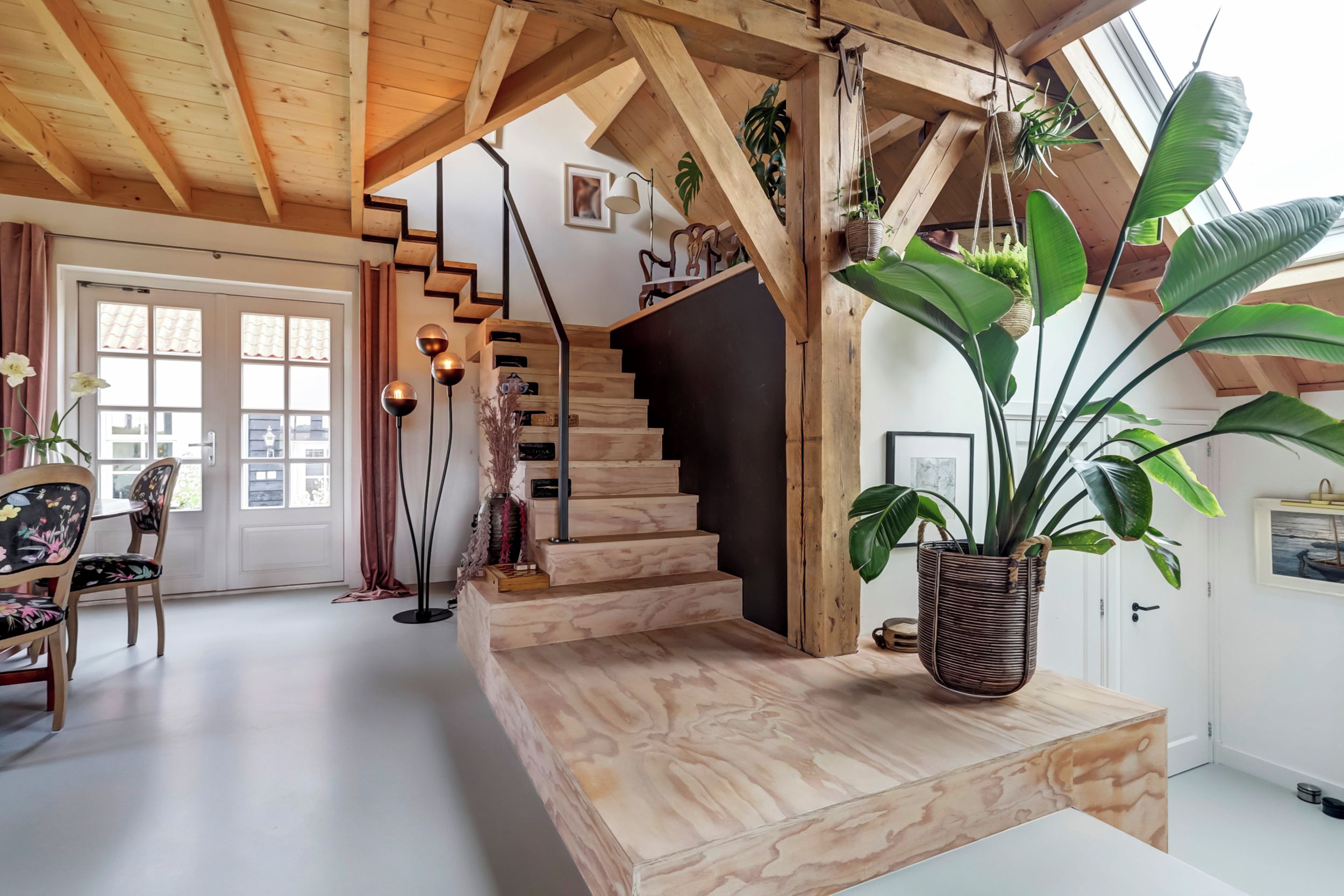 Eine Holzt Treppe mit einer schwarzen Wand unten, einer hängenden Pflanze und einem Tisch mit einer Pflanze darauf.