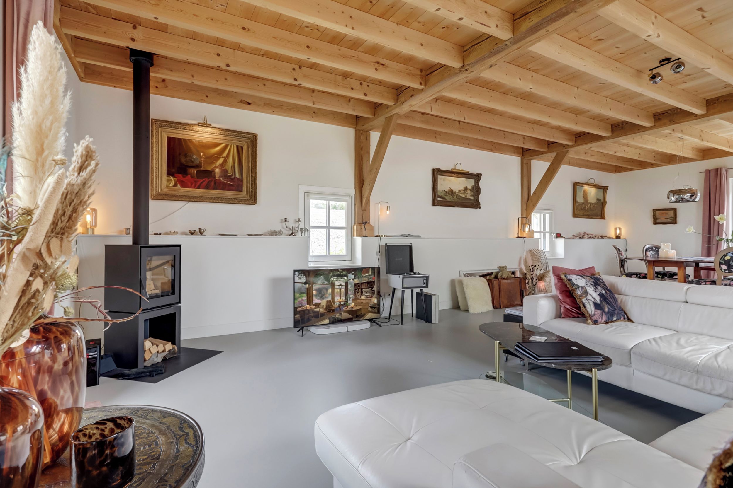 A spacious living room with a high ceiling, wooden beams, a fireplace, a television, and a sofa.