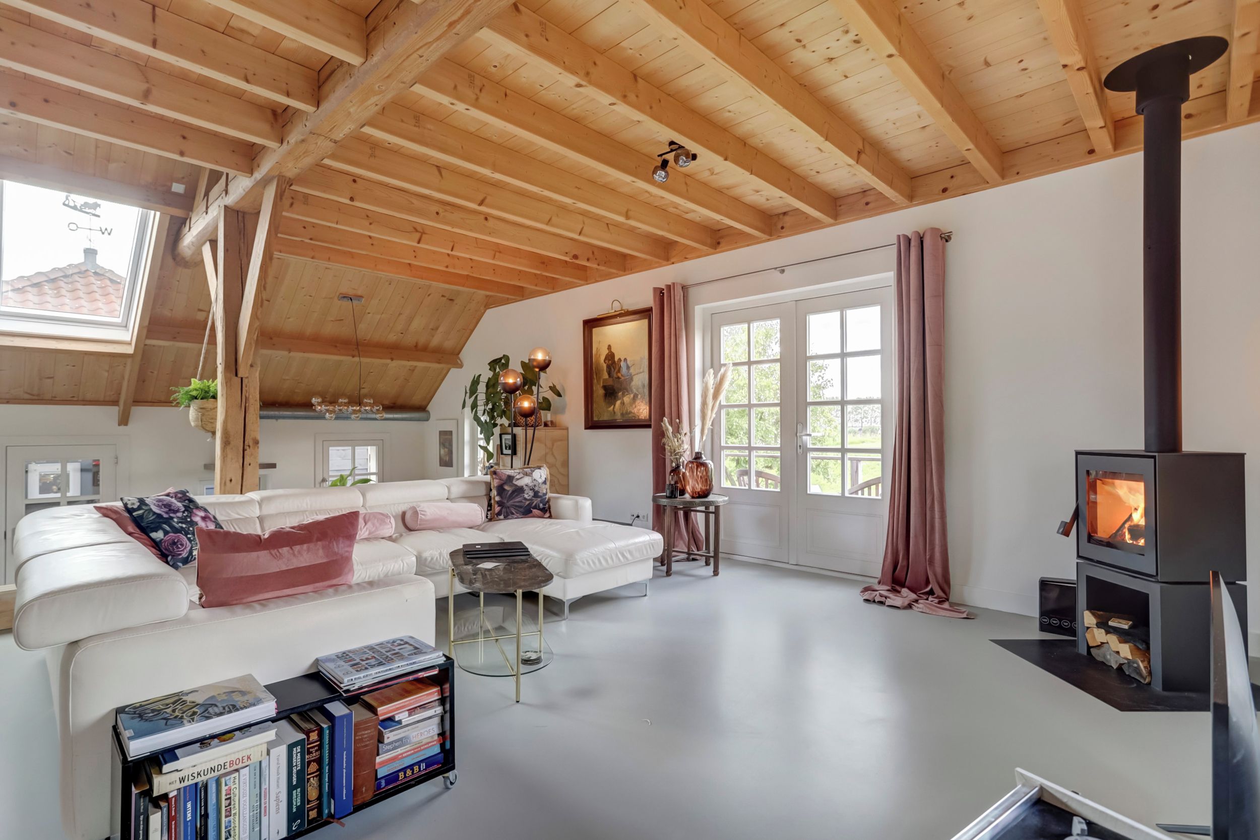 Ein großzügiges Wohnzimmer mit einem weißen Sofa, einem Couchtisch, einem Bücherregal, einem Kamin und einem großen Fenster mit Vorhängen.
